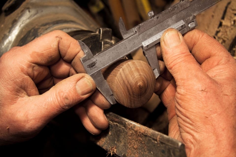 Hands measuring a turned wood piece with a caliper