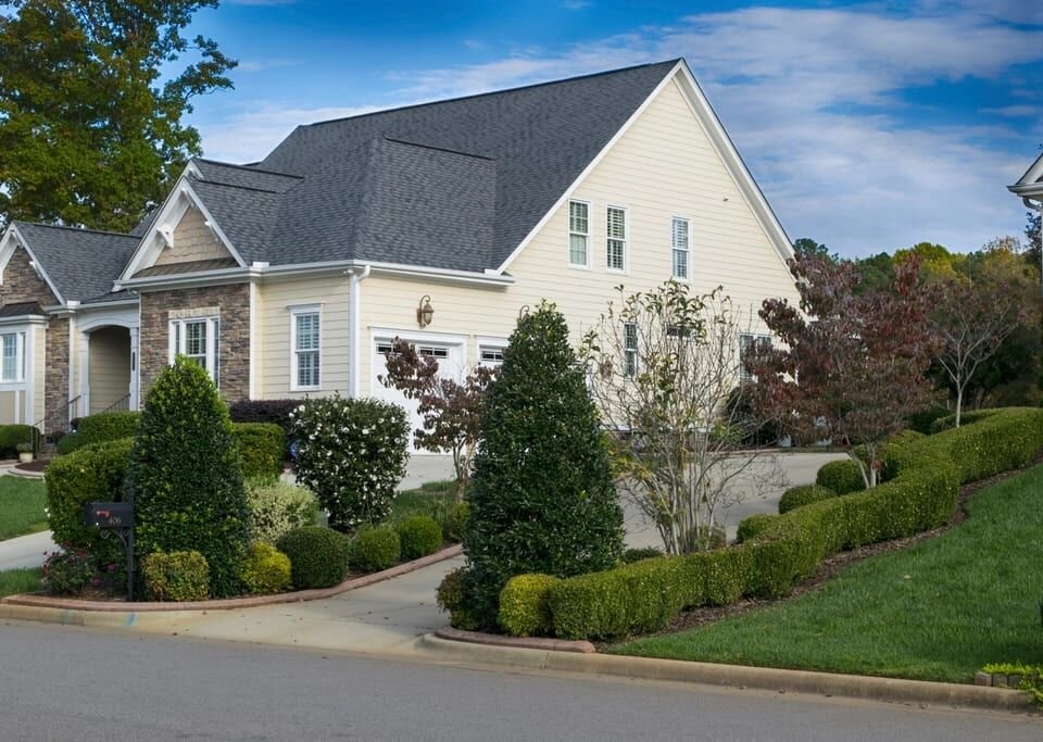 Light gray gabled home with manicured hedges and garden