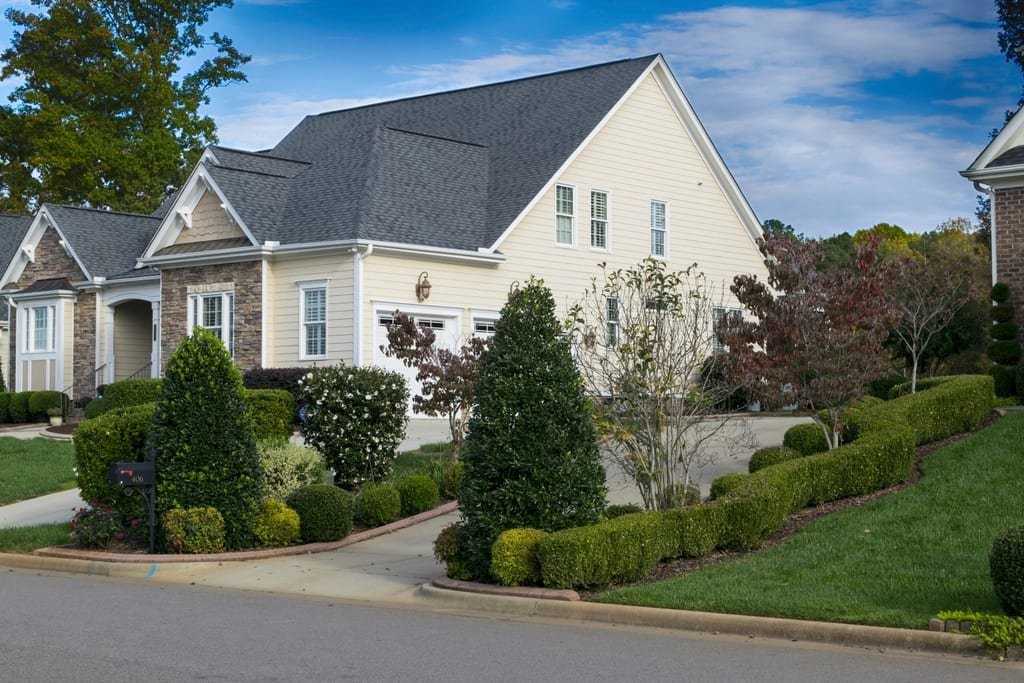 Light gray gabled home with manicured hedges and garden