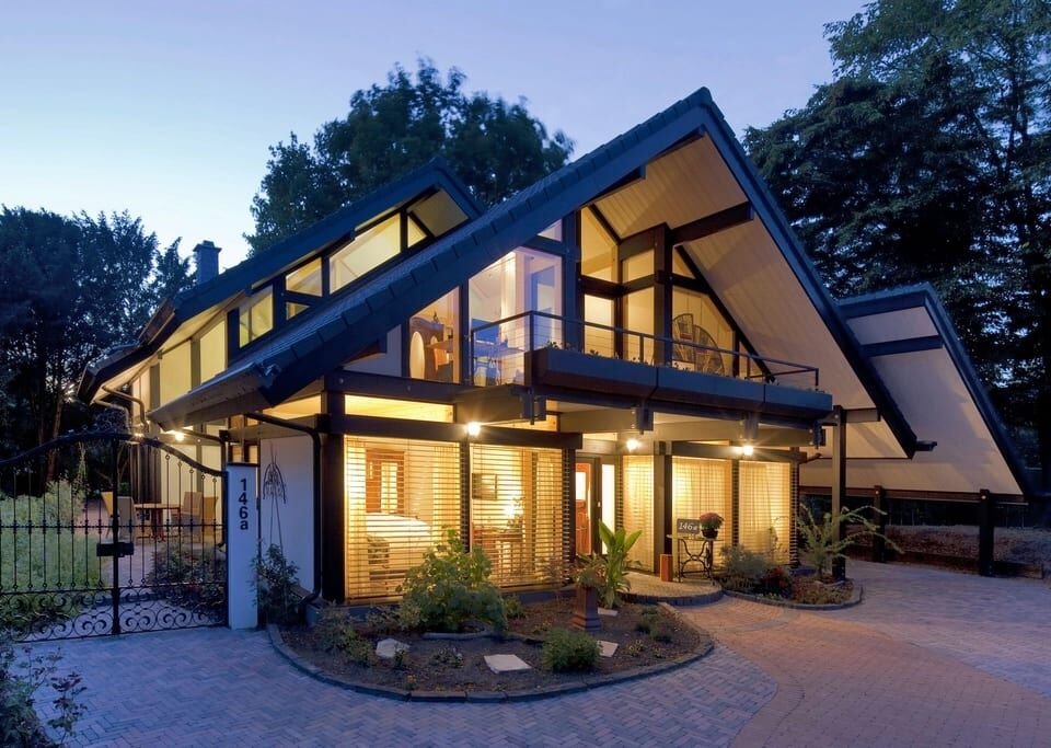 Modern two-story home with tall glass walls and warm lights at dusk