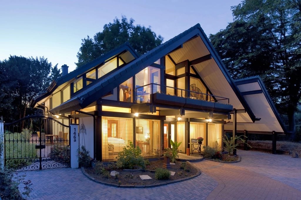 Modern two-story home with tall glass walls and warm lights at dusk