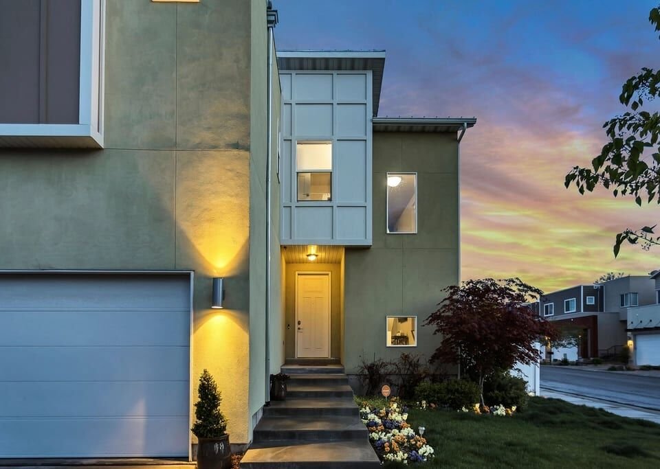 Contemporary home entrance with warm wall lights and a garage at twilight