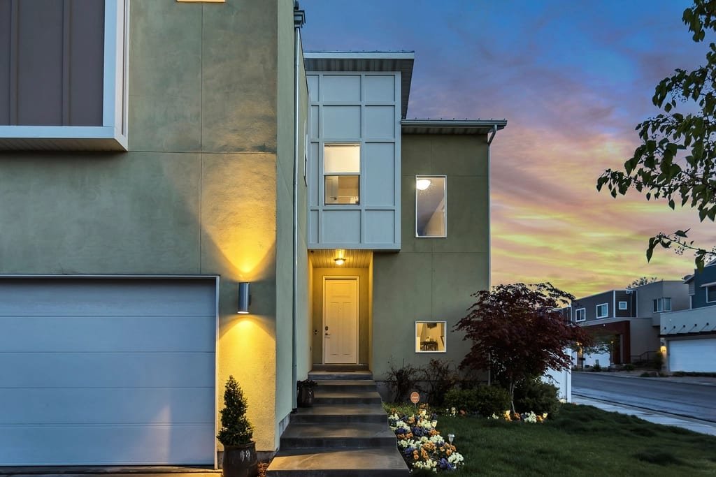 Contemporary home entrance with warm wall lights and a garage at twilight